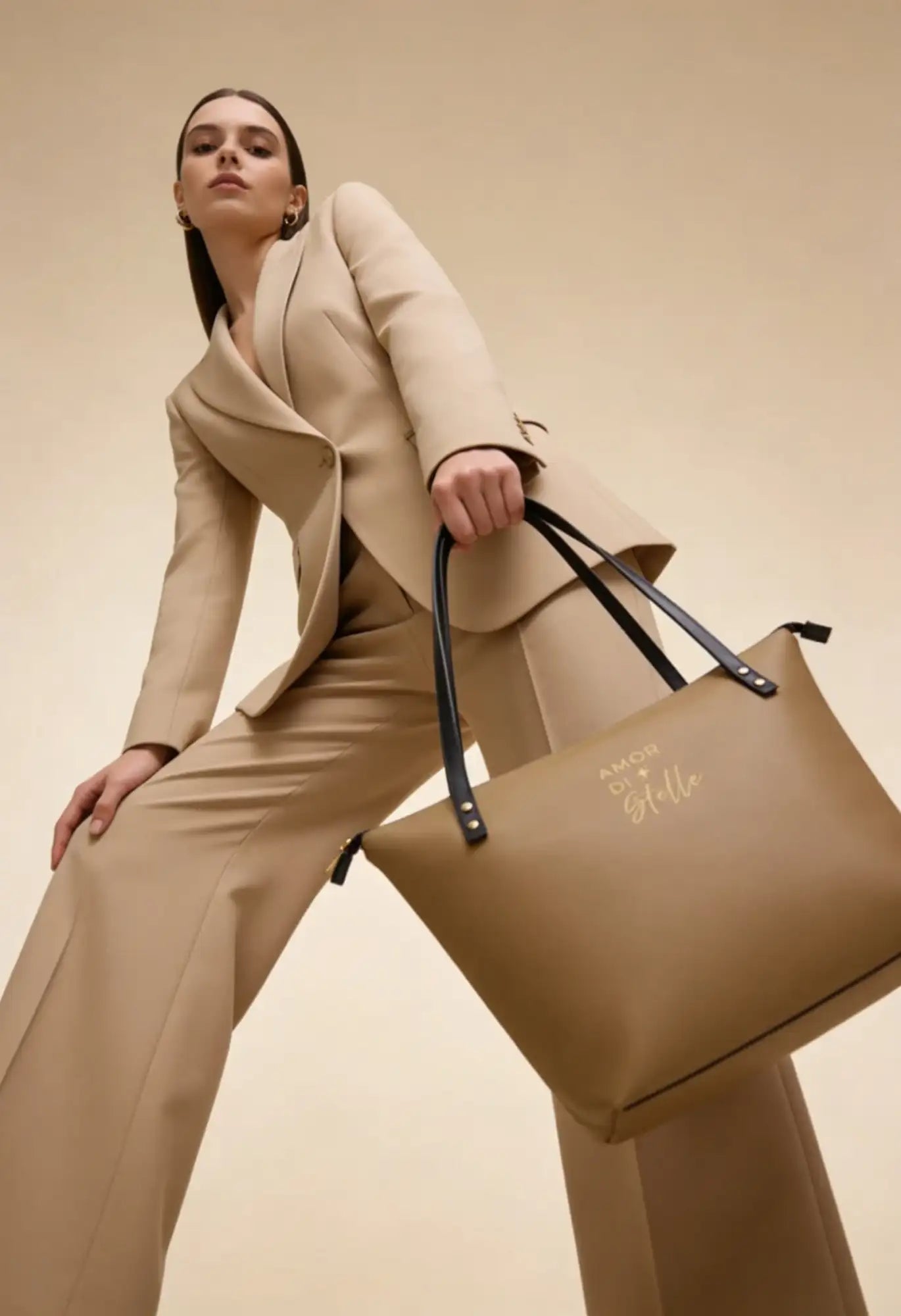 Beige Ledertasche mit schwarzen Tragegriffen und goldfarbener Prägung.