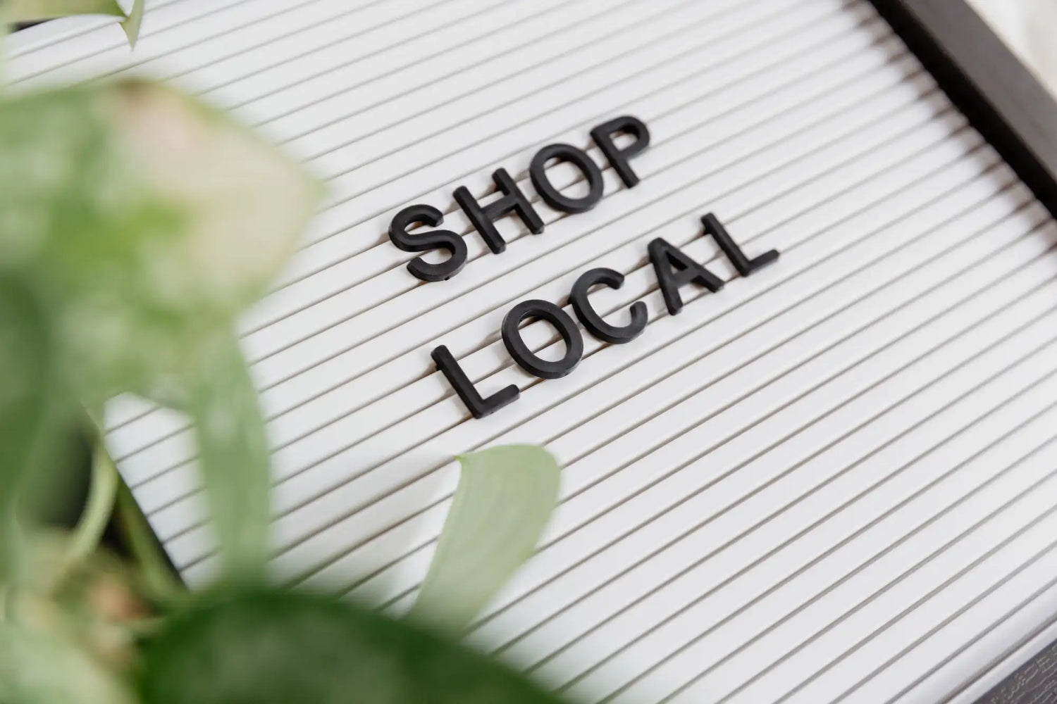 Schwarze 3D-Buchstaben-Kacheln, die „shop local“ auf einer weißen perforierten Tafel bilden.